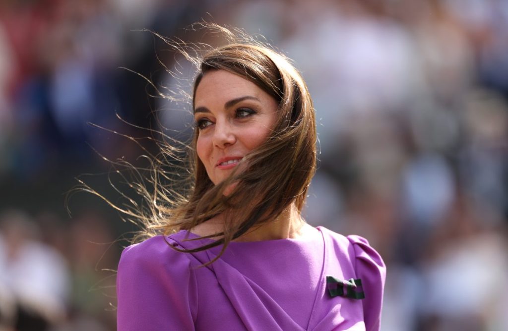 Kate Middleton at Wimbledon wearing a purple dress, her hair flowing in the wind.