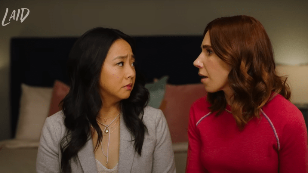 Ruby (played by Stephanie Hsu) and AJ (played by Zosia Mamet) look at each other with surprise and concern.