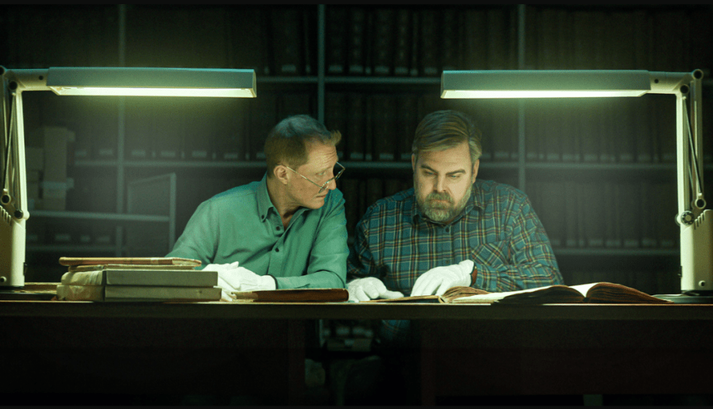 Photo from Netflix's The Breakthrough: Two men sit at a desk, examining genealogical records as they work to solve a cold case.