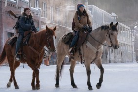 Two girls ride in the snow on horses.