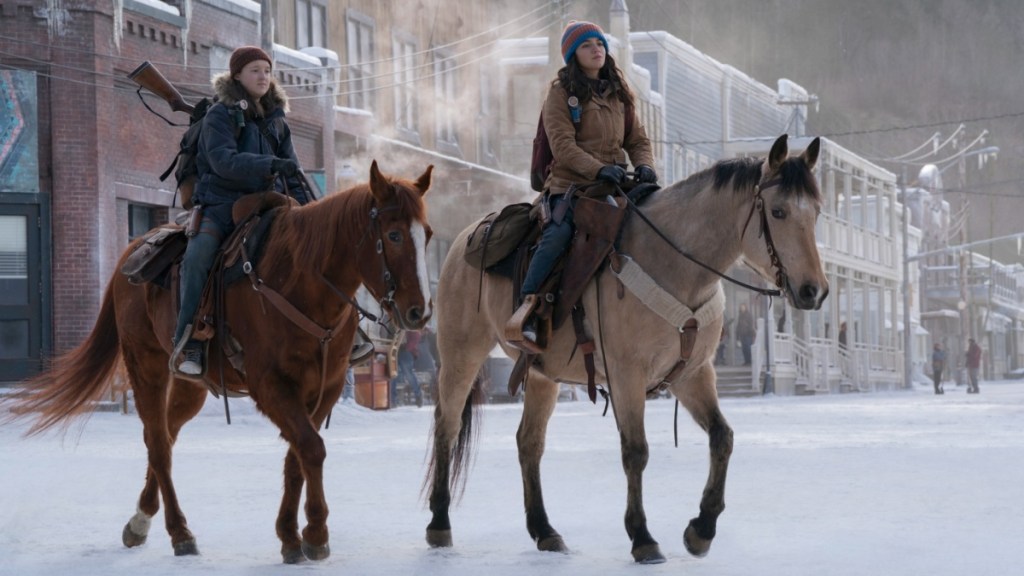 Two girls ride in the snow on horses.